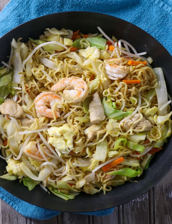 stir-fried ramen noodles with shrimp, chicken, and veggies in a pan.