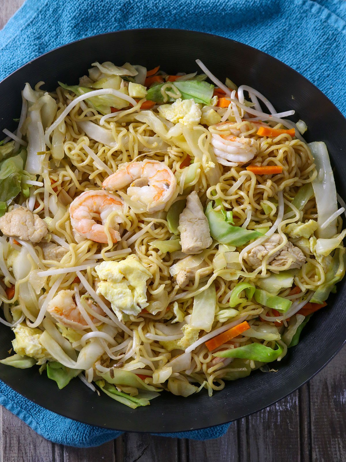 stir-fried ramen noodles with shrimp, chicken, and veggies in a pan.
