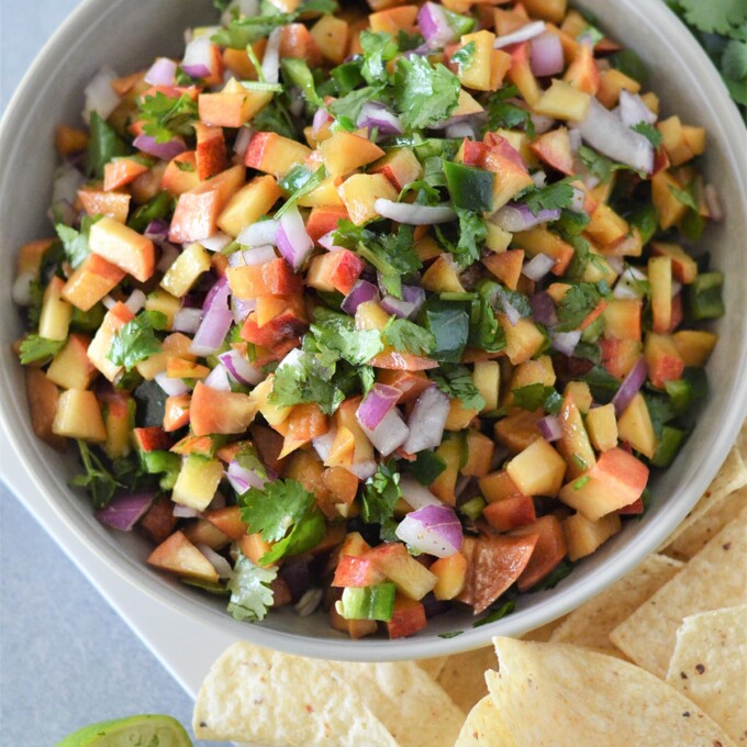 Nectarine Salsa in a white bowl with corns chips in the background.