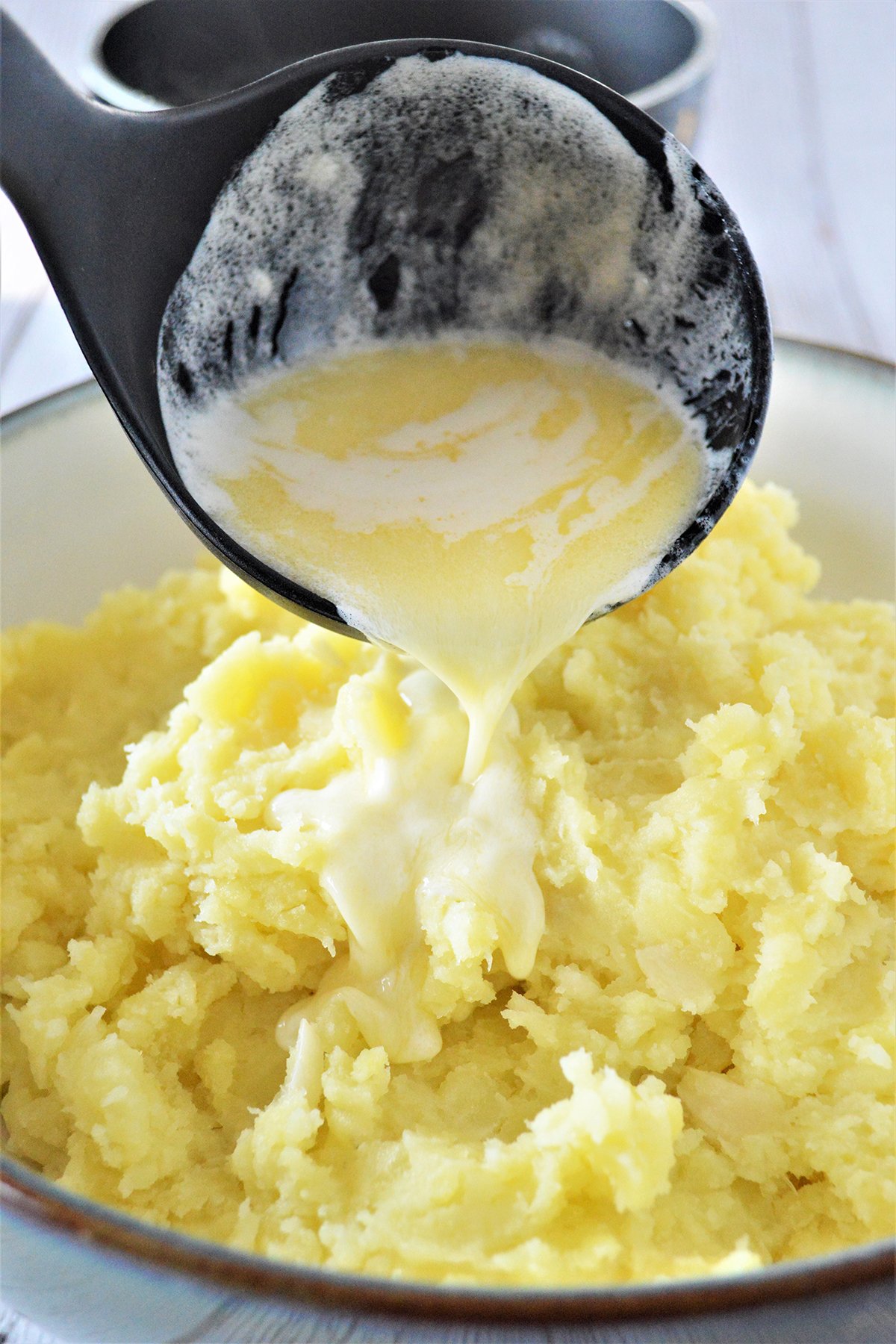 pouring heated heavy cream and butter mixture over mashed potatoes