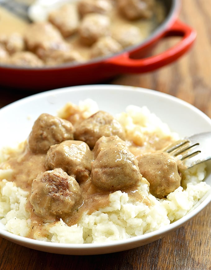 Swedish Meatballs with cream gravy over mashed potatoes on a white serving plate