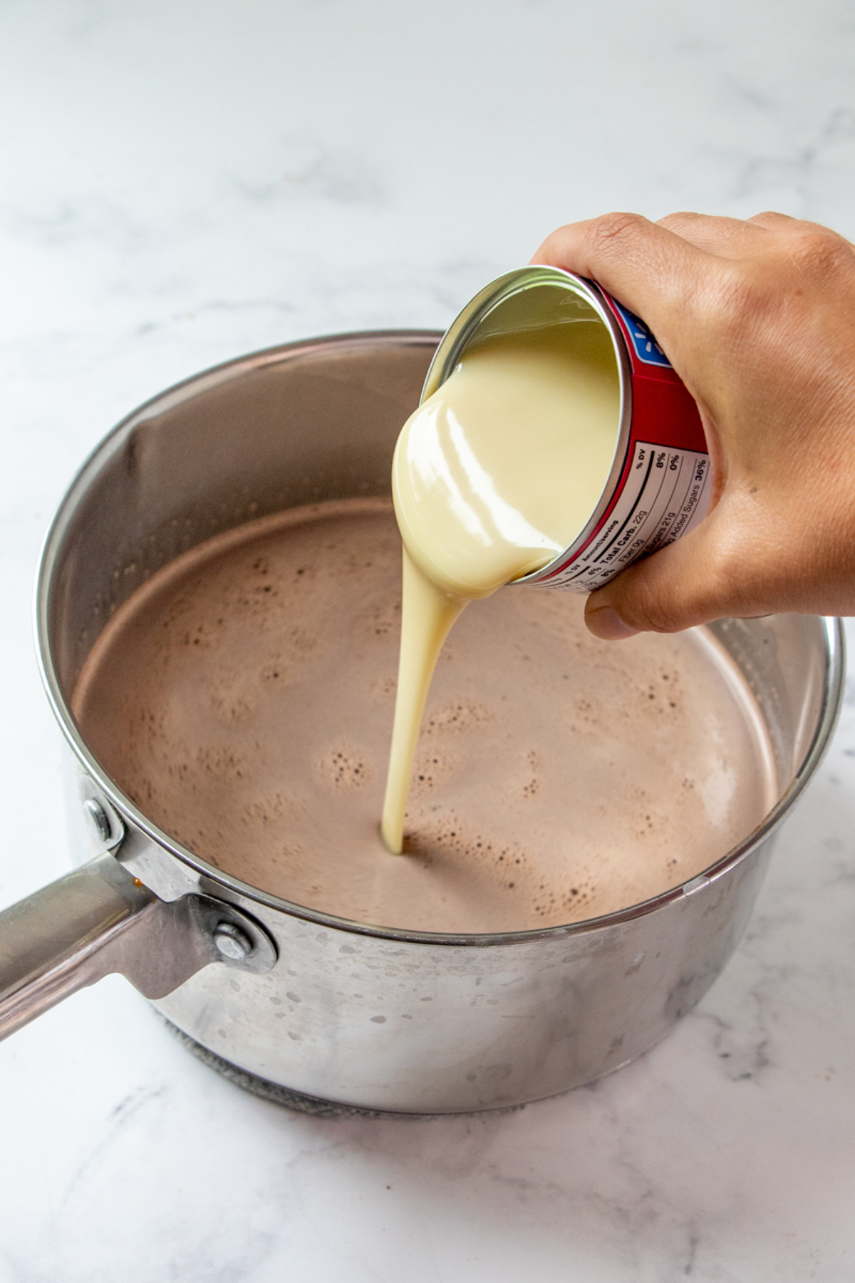 pouring a can of condensed milk into a pot of hot chocolate
