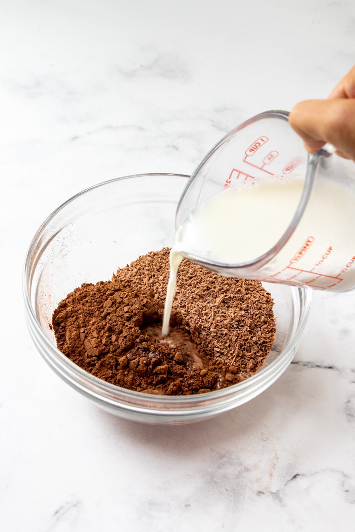 pouring milk into a bowl of grated chocolate and cocoa