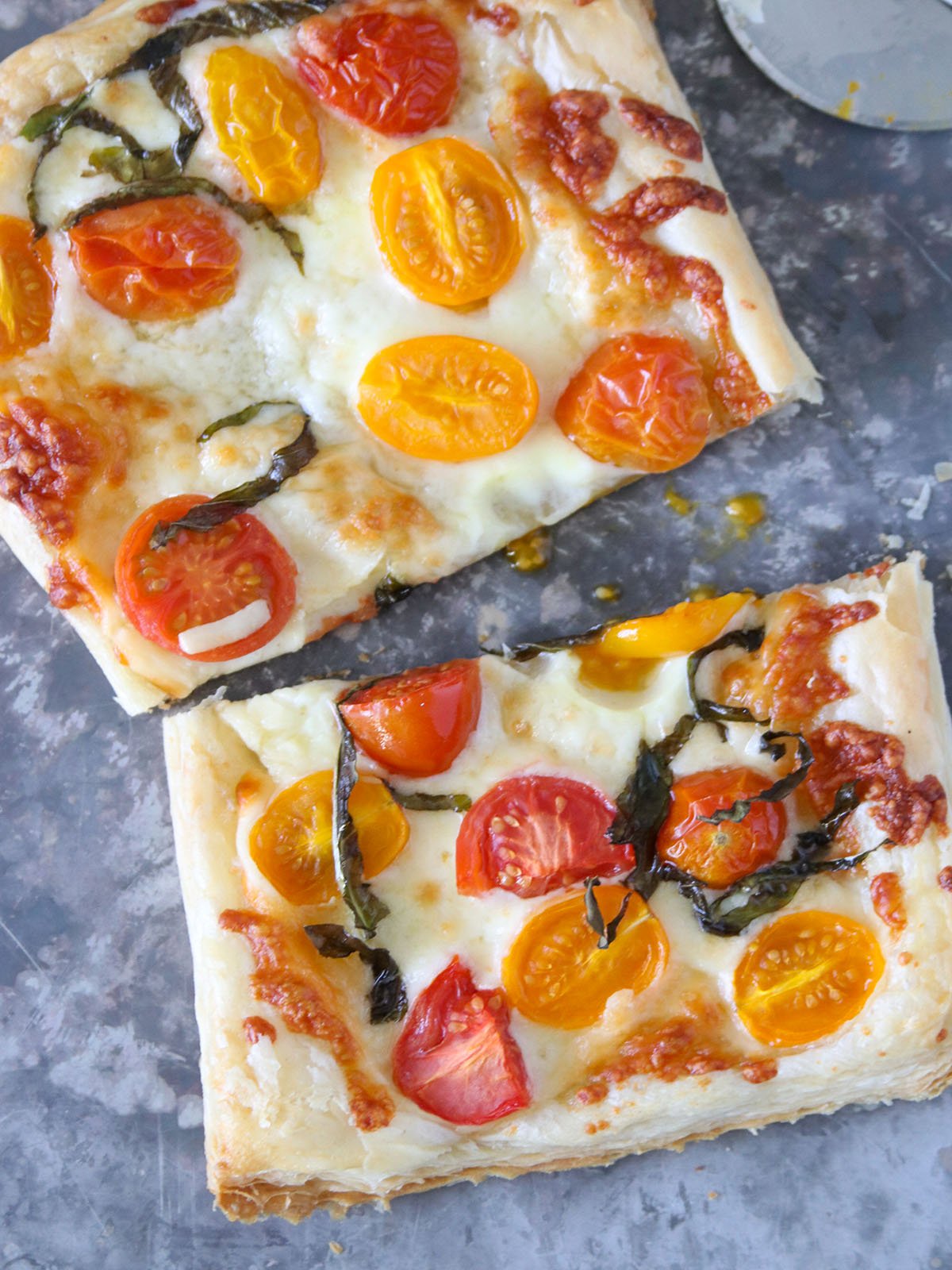 sliced puff pastry pizza with tomatoes, cheese, and basil topping