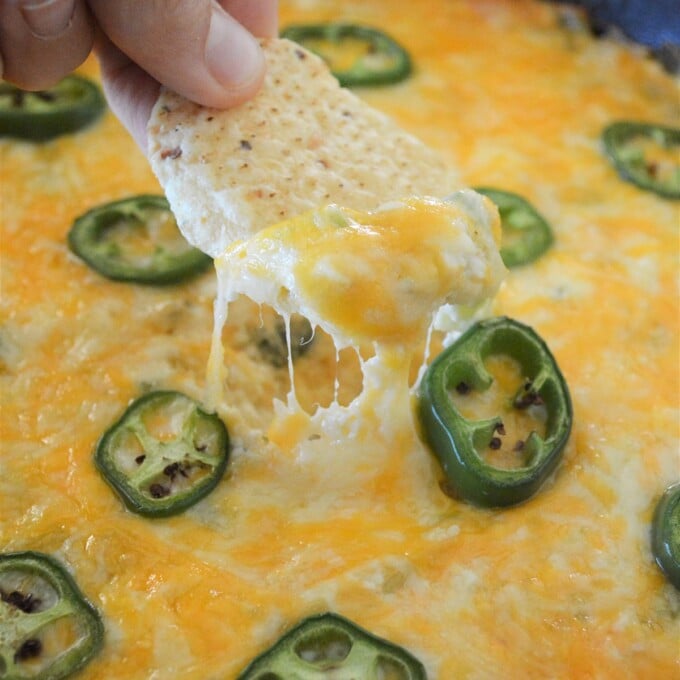 dipping corn chips in Cheesy Jalapeno Popper Dip baked in a cast iron skillet