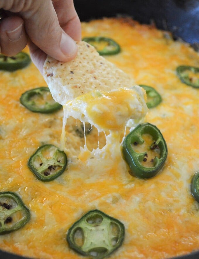dipping corn chips in Cheesy Jalapeno Popper Dip baked in a cast iron skillet