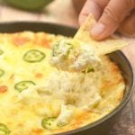 dipping corn chips in Cheesy Jalapeno Popper Dip baked in a cast iron skillet