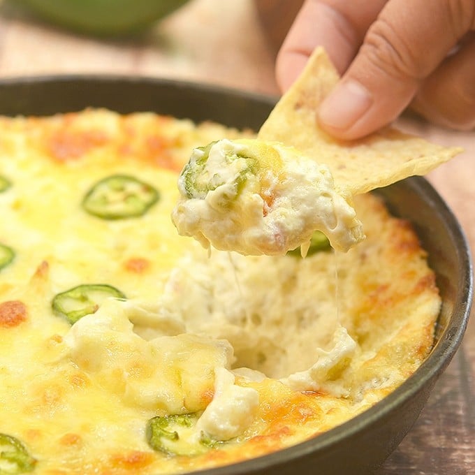 dipping corn chips in Cheesy Jalapeno Popper Dip baked in a cast iron skillet