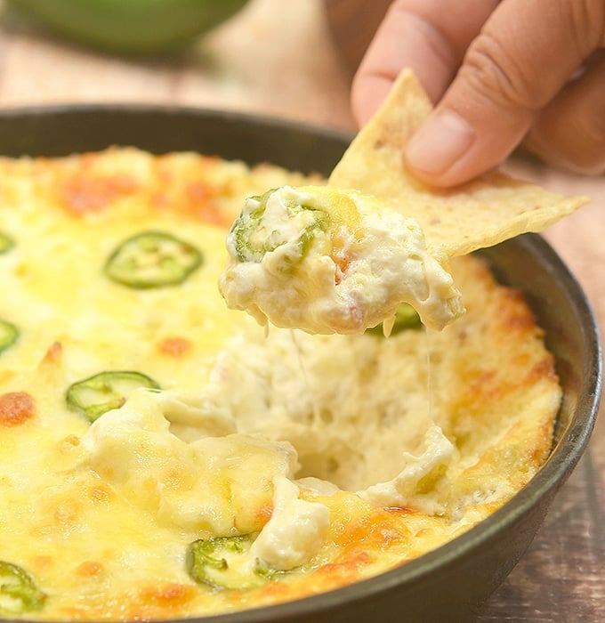 dipping corn chips in Cheesy Jalapeno Popper Dip baked in a cast iron skillet