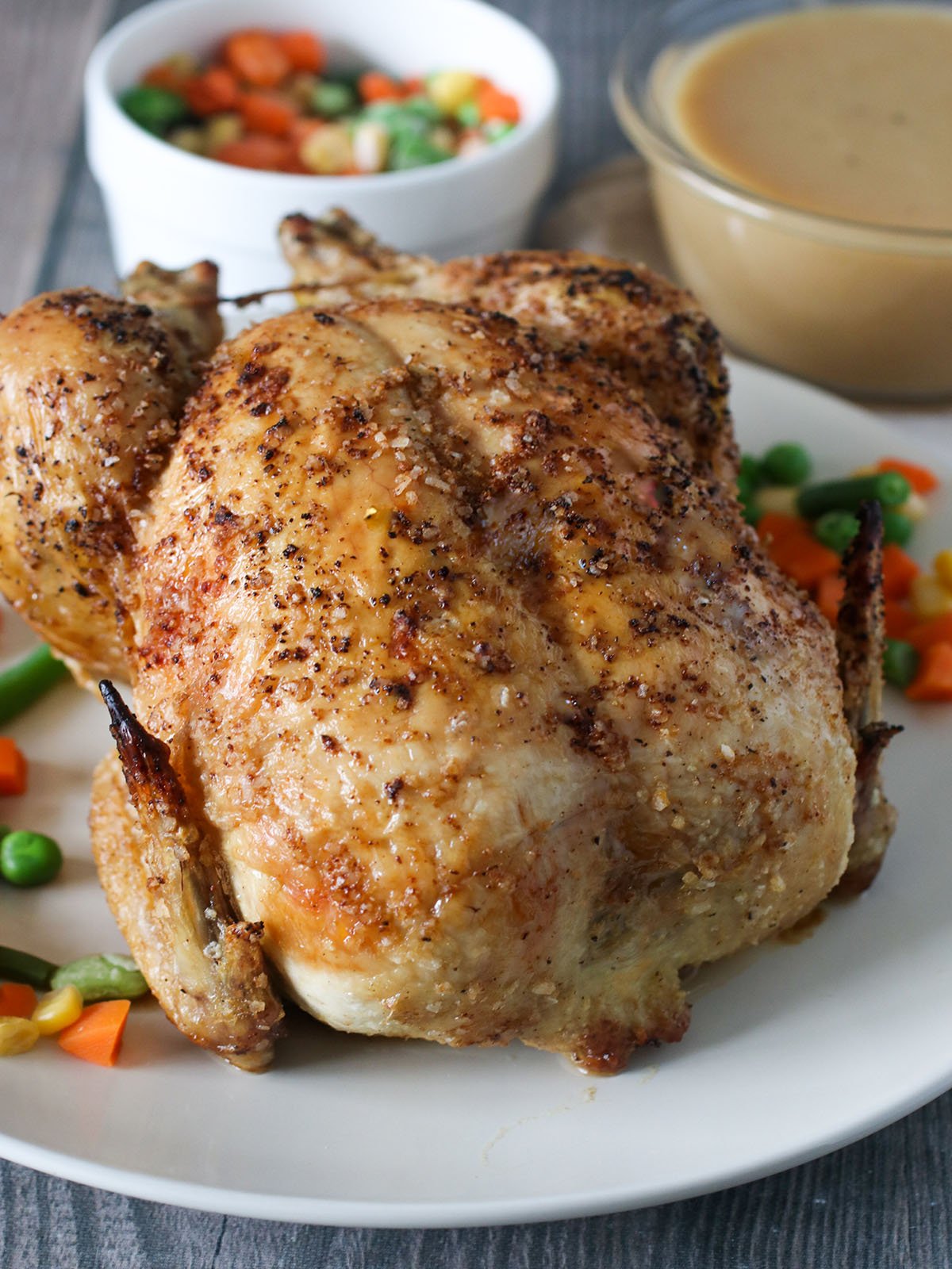 roasted chicken on a platter with veggies and gravy on the side