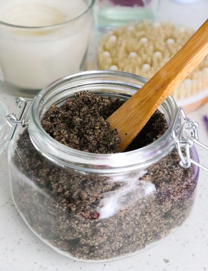 coffee sugar scrub in glass jar with candles and body brush on the side