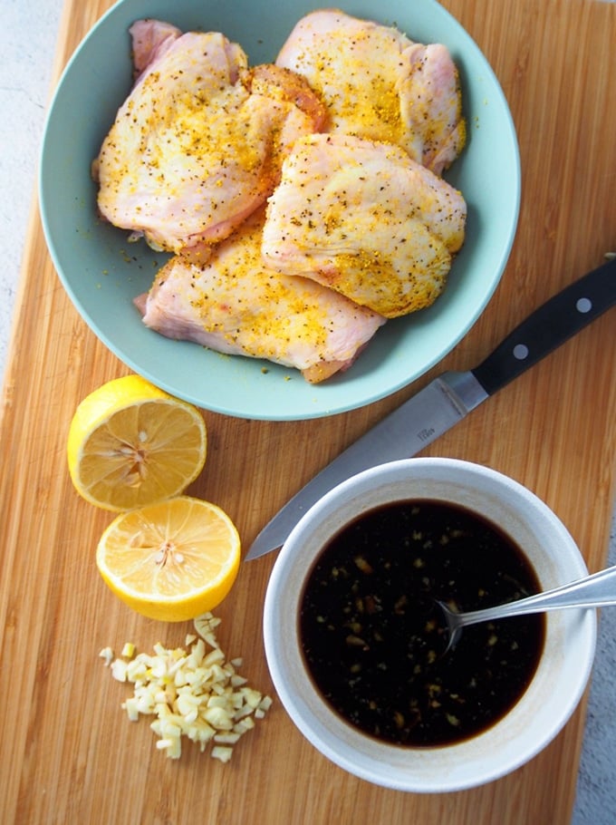 seasoned chicken thighs, sliced lemon, soy sauce marinade,, and minced garlic on a cutting board