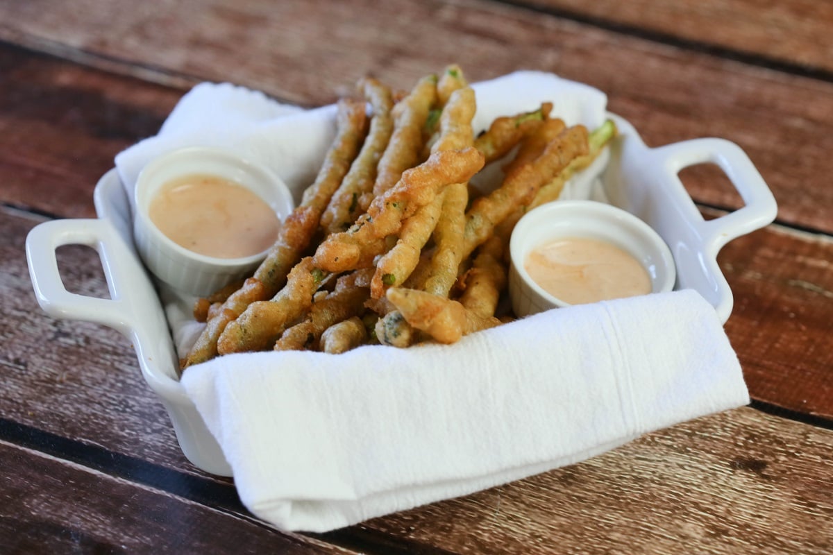 fried asparagus with beer batter in a white serving dish with bowls of dipping sauces