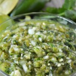 Salsa Verde in a glass bowl with jalapeno and cilantro in the background.