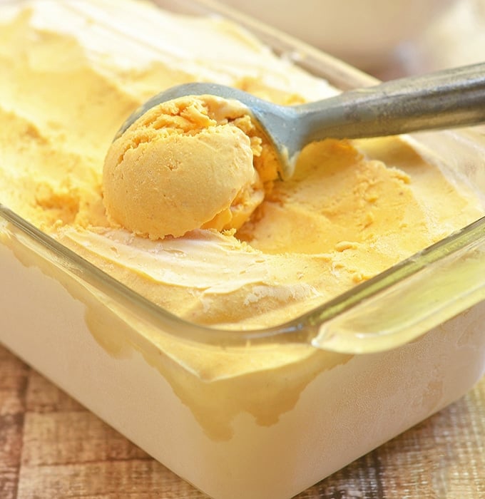 scooping pumpkin ice cream from a glass container