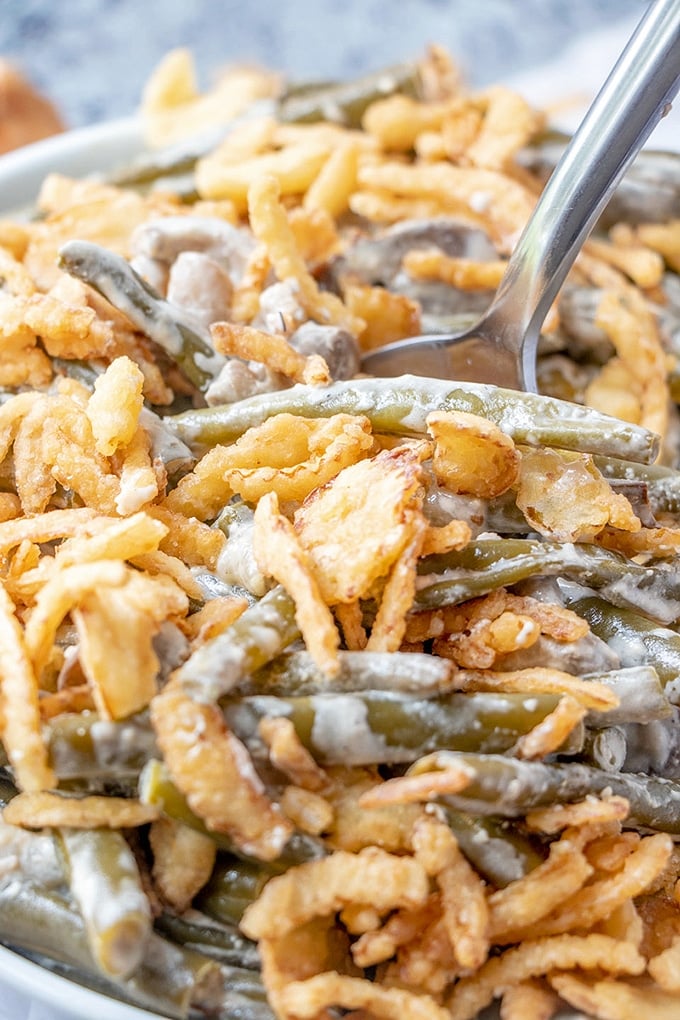 stirring green beans with crispy fried onions, mushrooms, and cream sauce with a fork