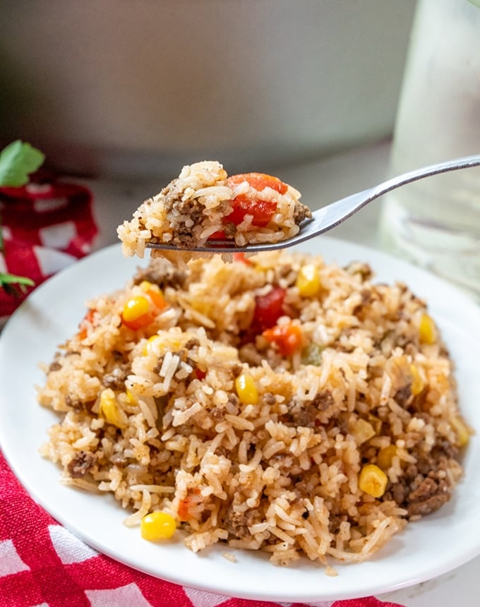 eating beef and rice casserole with a spoon from a white plate