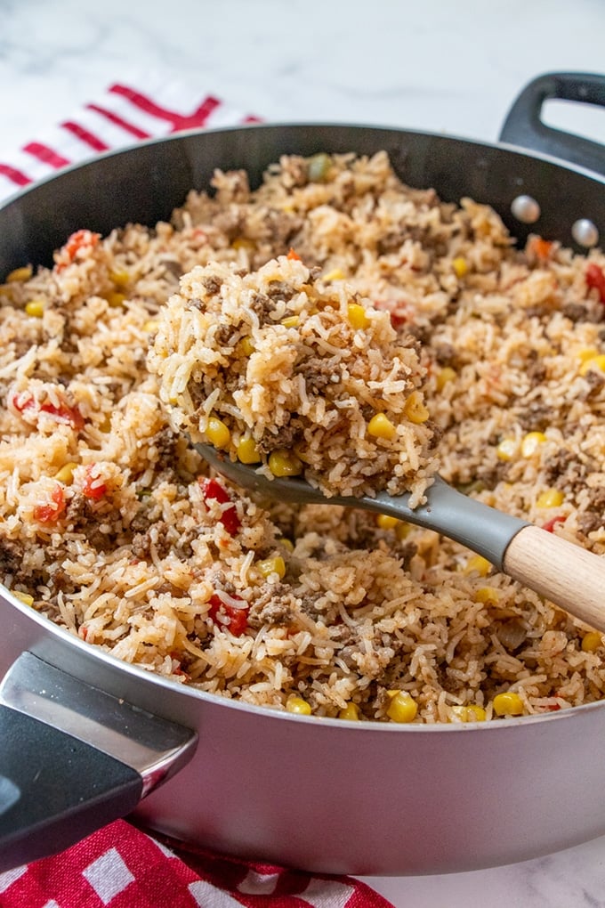 serving beef and rice casserole with a large spoon from a pan