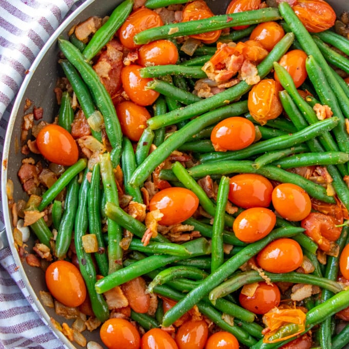 sauteed green beans in a pan with tomatoes and bacon