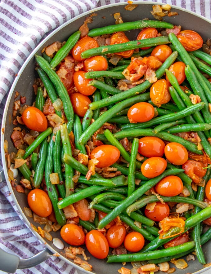 sauteed green beans in a pan with tomatoes and bacon