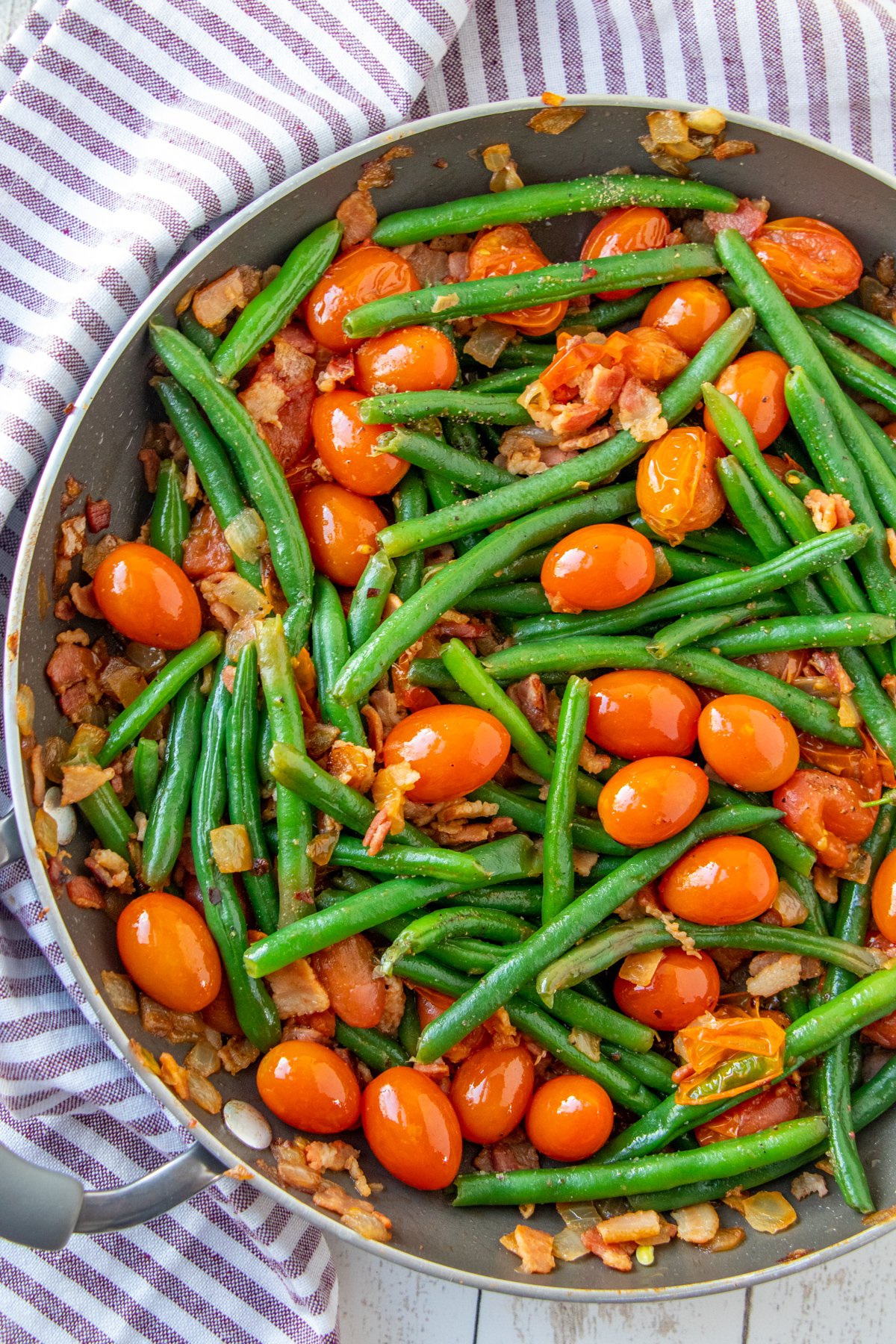 sauteed green beans in a pan with tomatoes and bacon