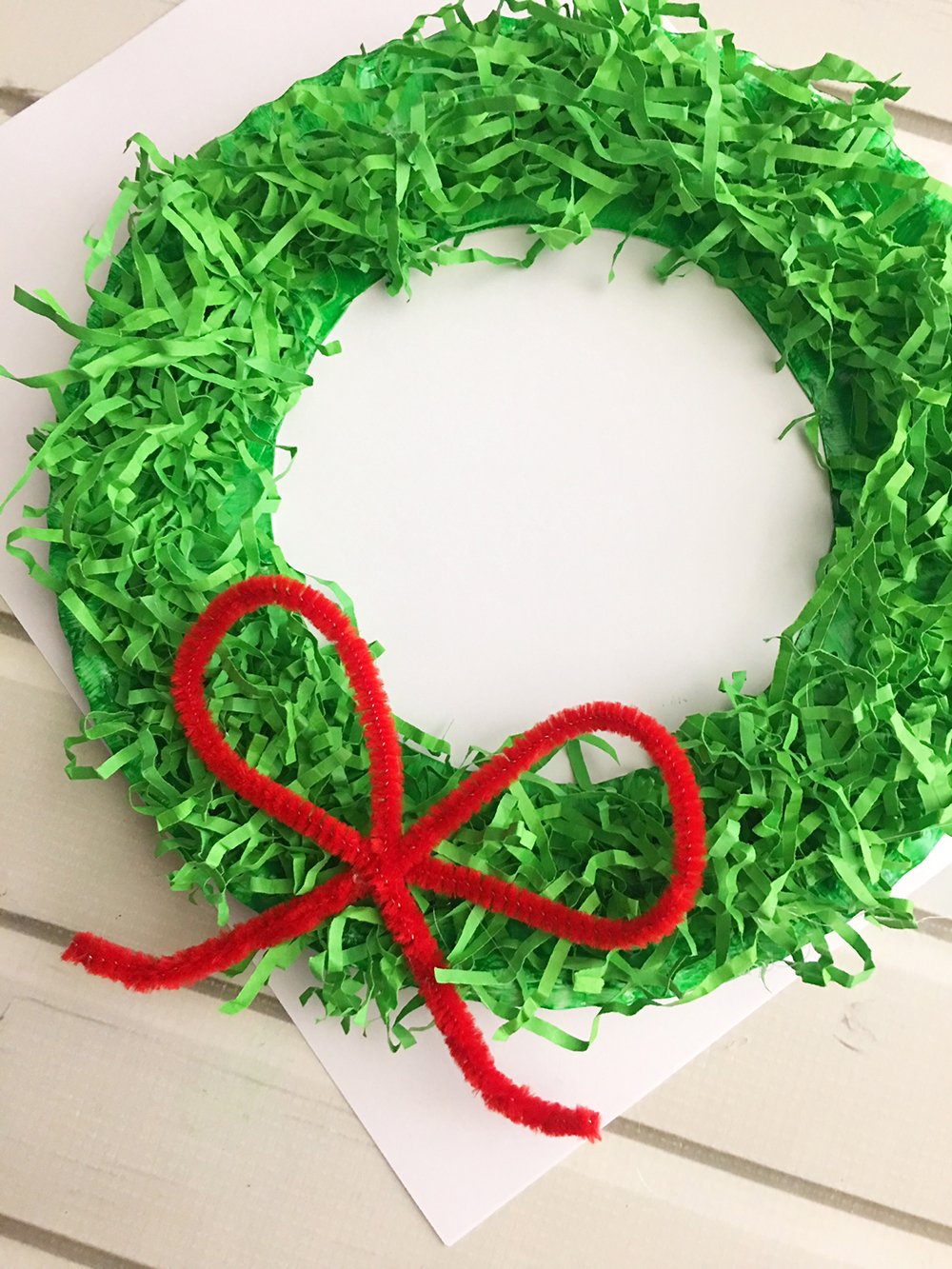 DIY Paper Christmas Wreath made with paper plate and shredded crinkle paper adds a festive touch to your holiday decor-Glue the pipe cleaner bow to the bottom center of the paper wreath.