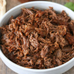 barbacoa beef in a white bowl with a mason jar of sauce on the side