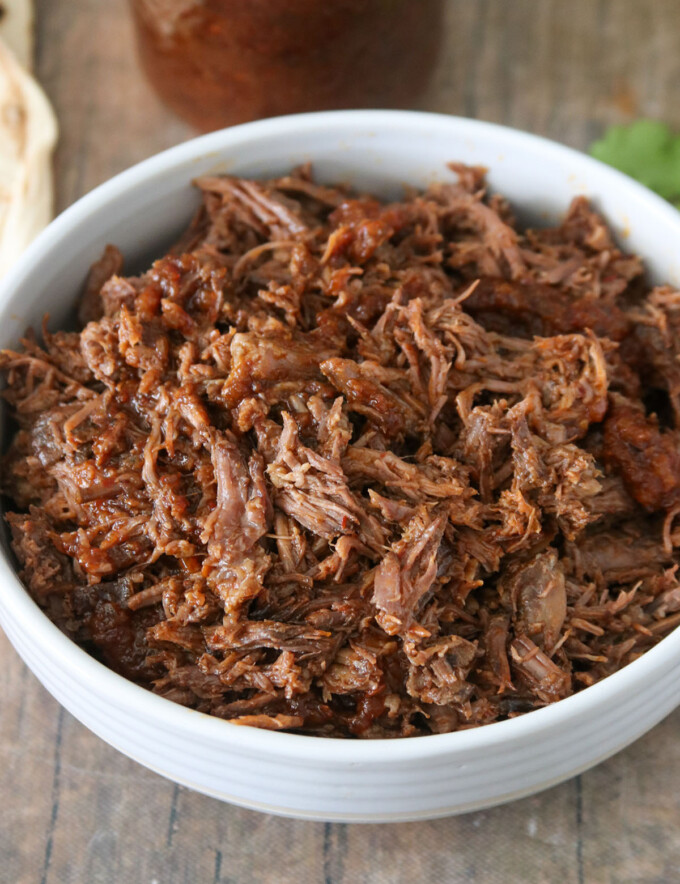 barbacoa beef in a white bowl with a mason jar of sauce on the side