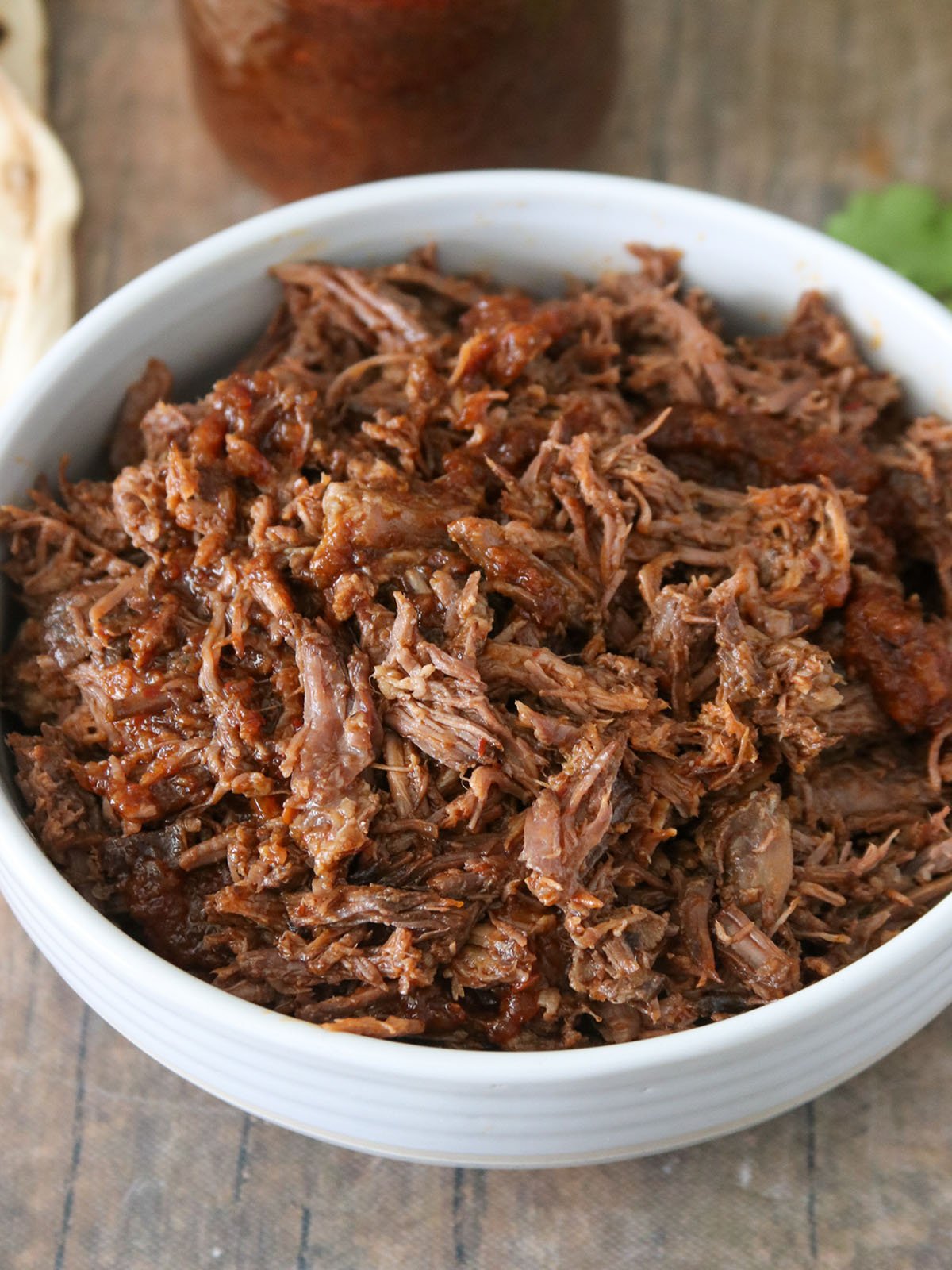 barbacoa beef in a white bowl with a mason jar of sauce on the side