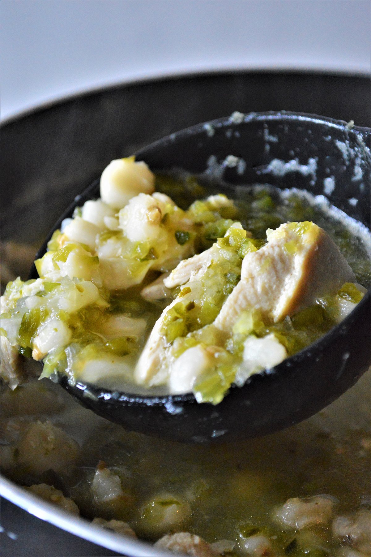 serving pozole verde from a pot with a ladle
