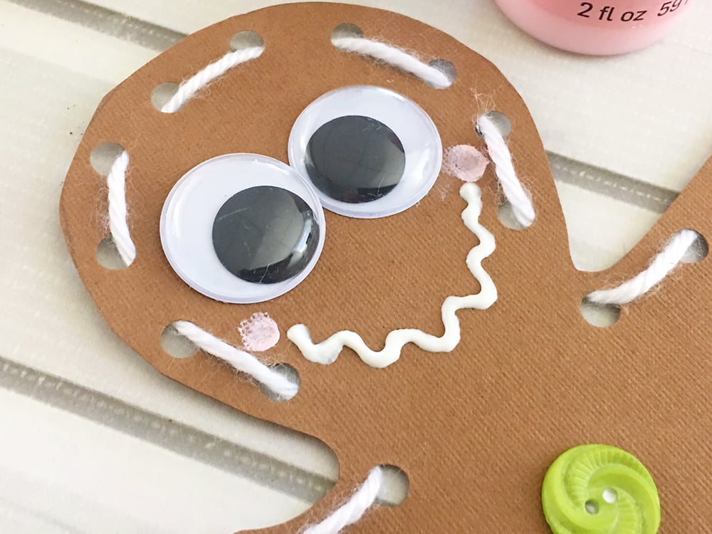 DIY Gingerbread Man Ornaments - Draw a wavy smile under the eyes using the puffy paint and dot the cheeks with a dab of pink paint.