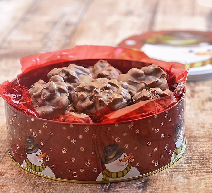 Slow Cooker Chocolate Peanut Clusters in red Christmas snowman tin