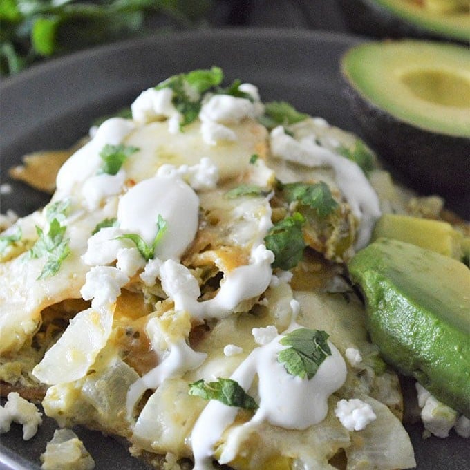 Chilaquiles with Salsa Verde topped with sour cream and chopped cilantro with avocado slices on the side on a plate