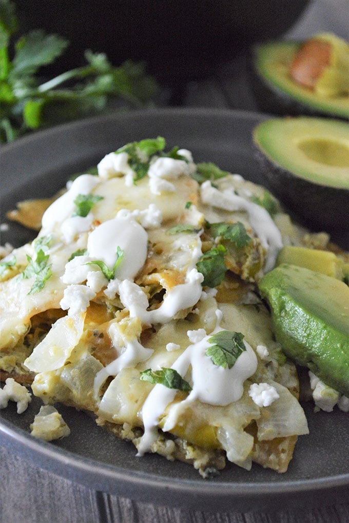 Chilaquiles with Salsa Verde topped with sour cream and chopped cilantro with avocado slices on the side on a plate