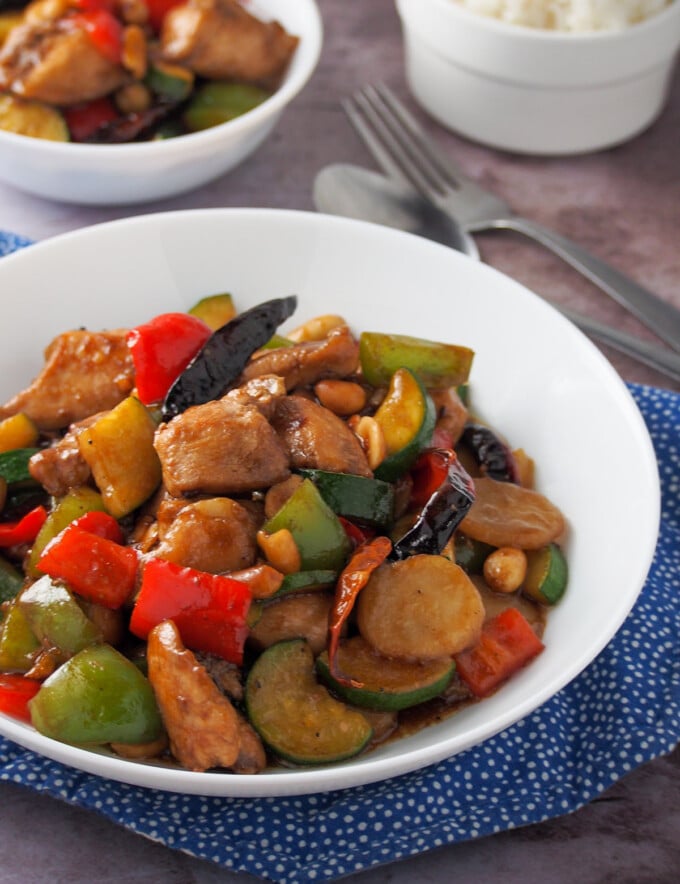 stir-fried kung pao chicken in a white bowl with a bowl of steamed rice on the side