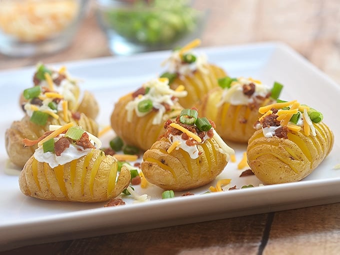 Mini Hasselback potatoes topped with sour cream, bacon, and green onions