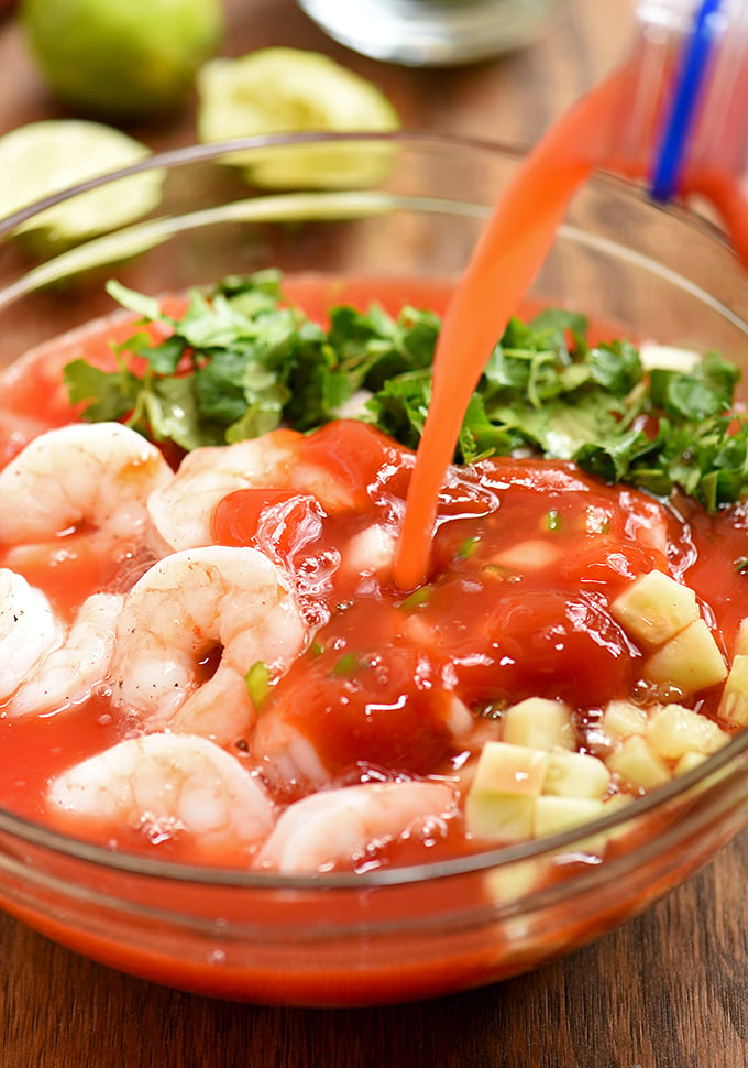 pouring Clamato juice to a bowl of coctel de camarones