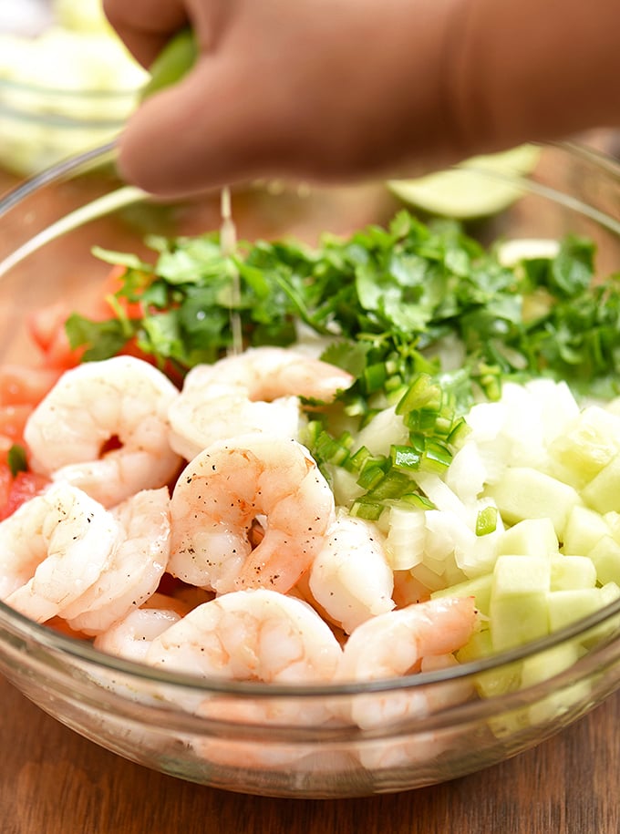 squeezing lime juice on a bowl of shrimp, cucumber, tomatoes, onion, cilantro, and chili peppers for coctel de camarones