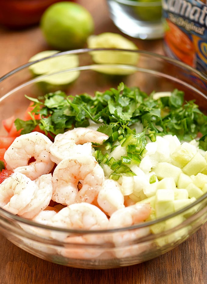 cooked shrimp, tomatoes, cucumber, onions, cilantro, and chili peppers in a clear bowl for Mexican-style shrimp cocktail