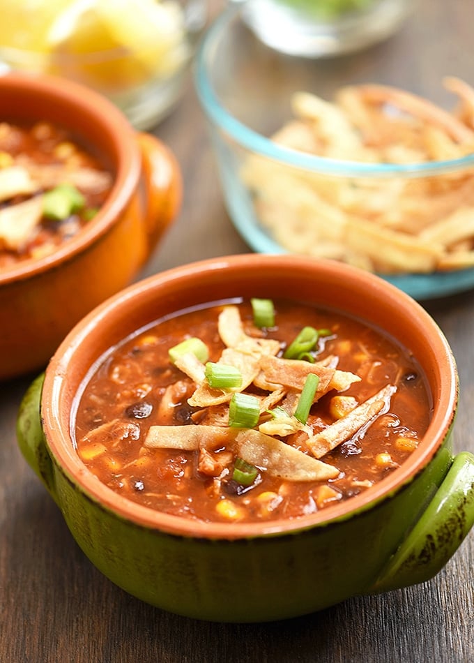 easy chicken tortilla soup in green bowl with a side of crisp tortilla and lemon slices