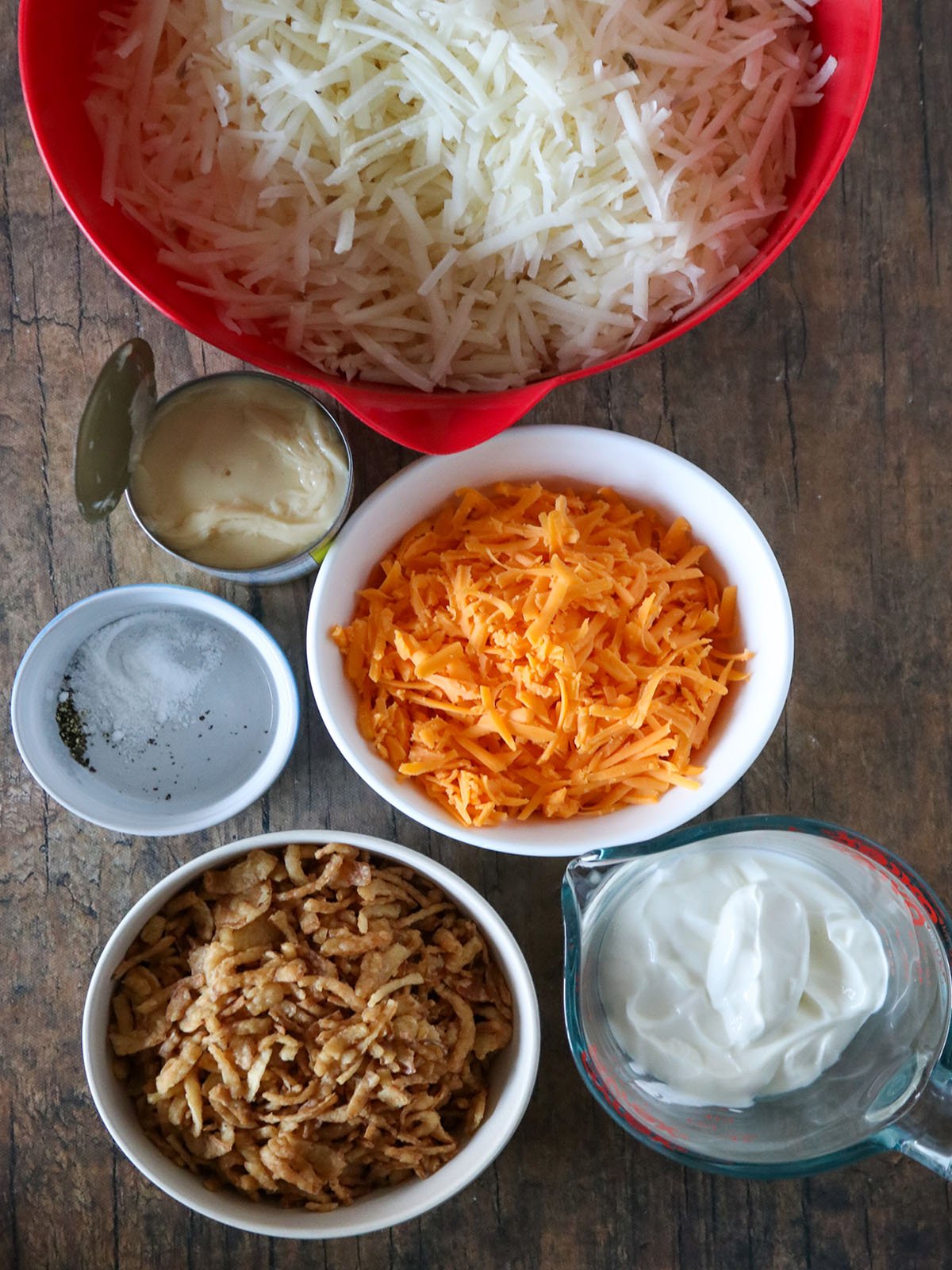 shredded hashbrown, shredded cheese, sour cream, can of condensed soup, crispy onion strings, ranch seasoning in bowls.