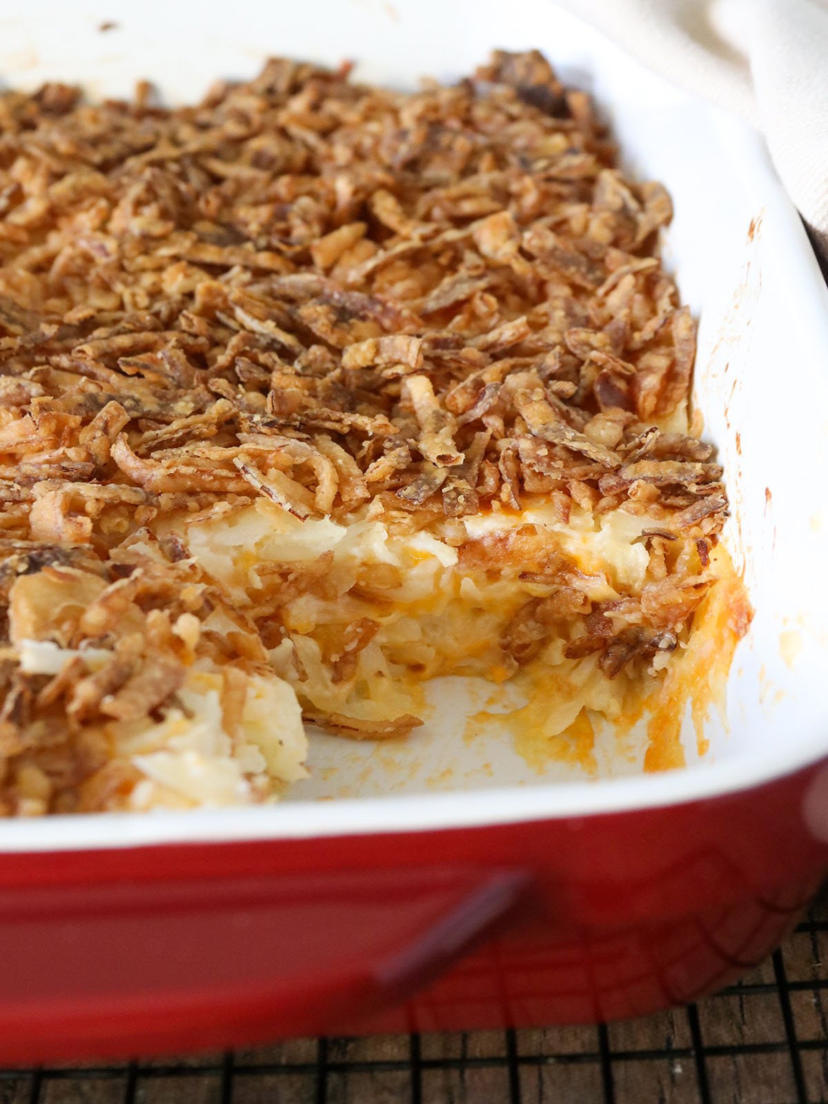 baked cheesy hashbrown casserole with crispy onion topping in a red casserole dish