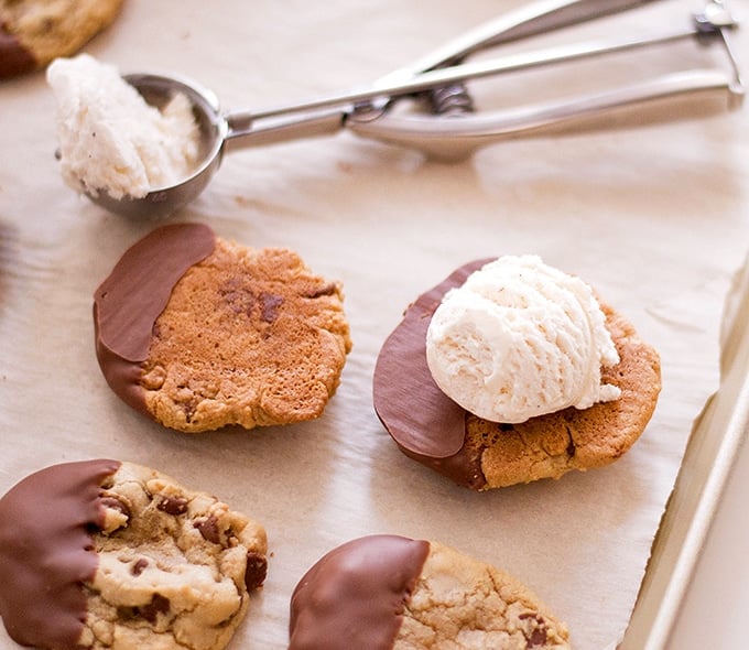 chocolate chip cookies half-coated in milk chocolate topped with vanilla ice cream to make ice cream sandwiches