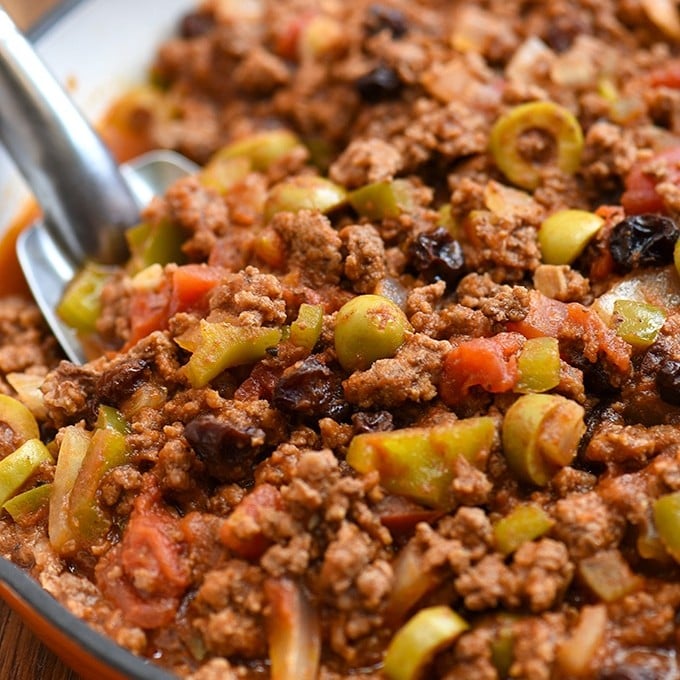 Cuban-style picadillo recipe with green olives, raisins, bell peppers, and tomato sauce in a skillet