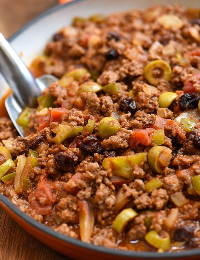 Cuban-style picadillo recipe with green olives, raisins, bell peppers, and tomato sauce in a skillet