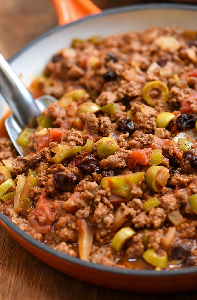 Cuban-style picadillo recipe with green olives, raisins, bell peppers, and tomato sauce in a skillet