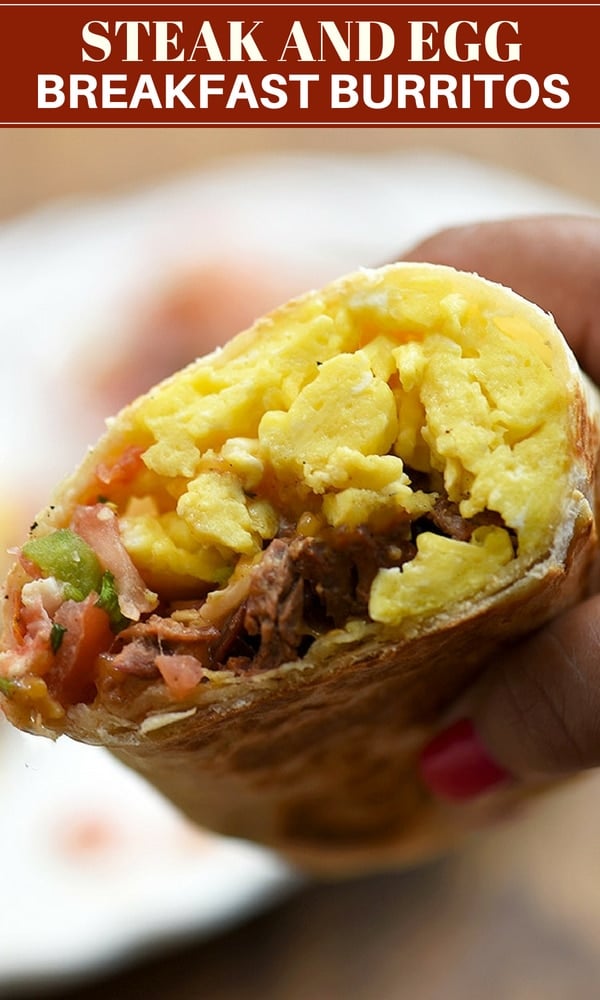 hand holding a breakfast burrito half filled with steak, eggs, and tomato salsa