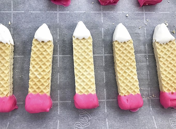 pencil=shaped sugar wafers coated in pink and white candy melts on a parchment-lined baking sheet