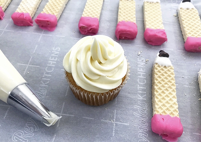 frosted vanilla cupcakes with pencil shaped sugar wafer cookies on the side