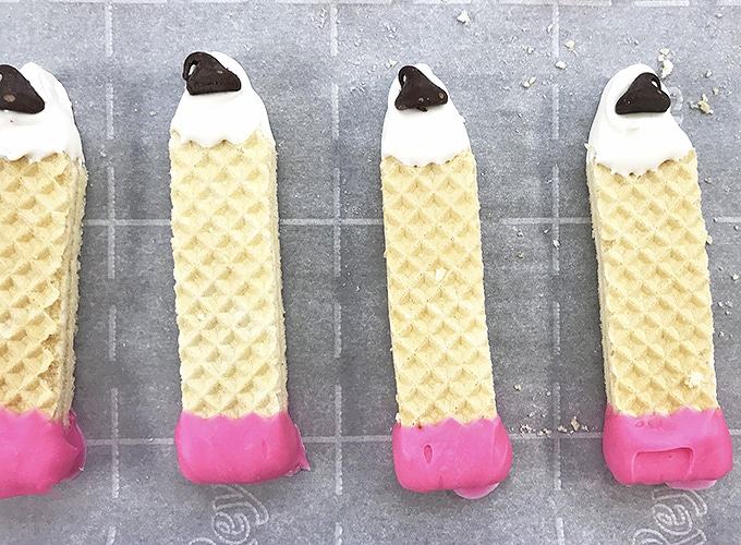 pencil design sugar wafers coated with pink and white chocolate on a baking sheet